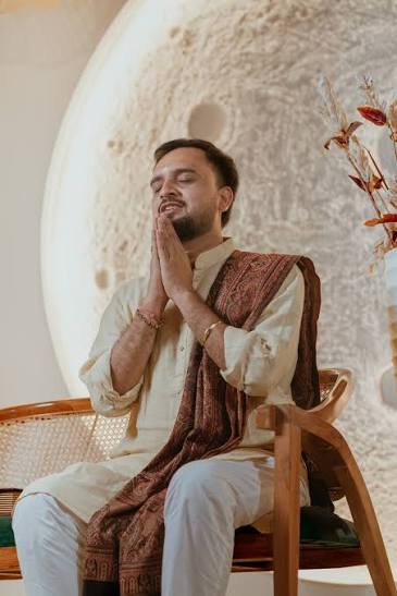 Serene mentor in cream kurta and paisley shawl, eyes closed in meditation